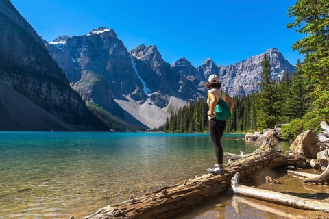 Female hiker standing on a log, admiring the stunning turquoise waters of moraine lake and the
