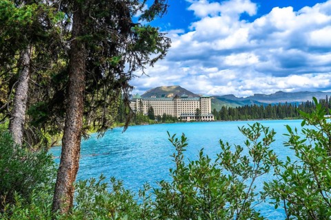 Lush vegetation framing turquoise waters of lake louise reflects a luxury hotel against stunning