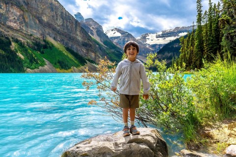 Happy child standing on a rock by the turquoise water of lake louise, enjoying the stunning scenery