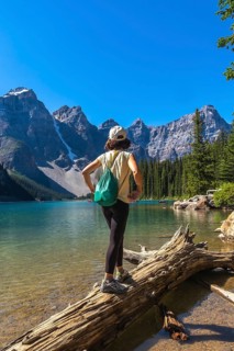 Female tourist standing on a log, admiring the turquoise waters of moraine lake, surrounded by the