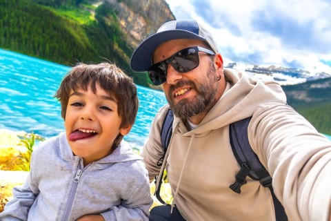 Father and son capturing a selfie by the turquoise waters of lake louise, surrounded by stunning