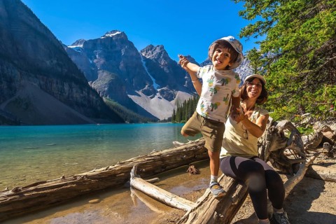 Mother and son are having fun while posing on a log by the turquoise waters of moraine lake,