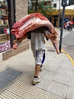 Man carries half of a cow on his shoulder. Beef is an important foodstuff in Argentina and is