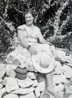 Portrait of young woman wearing summer dress sitting on stone wall holding straw hat, Malta,