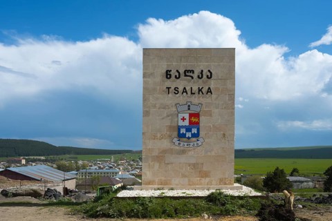 A monument with the coat of arms of Tsalka against a village backdrop and a blue sky, town sign