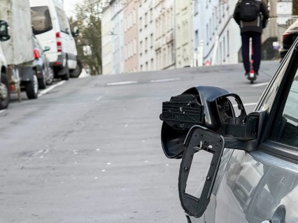 A car on the side of a steep residential street. The vehicle's left wing mirror is severely damaged