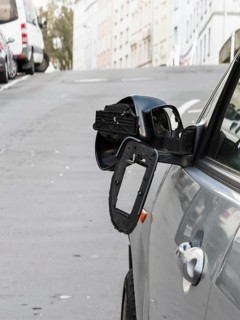 A car on the side of a steep residential street. The vehicle's left wing mirror is severely damaged