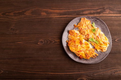 Baked chicken meat with cheese and tomatoes on brown wooden background. top view, flat lay, copy