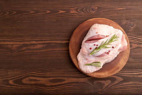 Raw Turkey Thigh with spices and rosemary on cutting board on brown wooden background. top view,