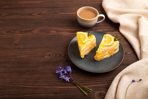 Lemon cake on brown wooden background and linen textile, cup of coffee, side view, copy space