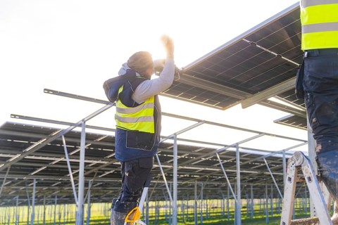 Worker installing solar panels in sunlight on metal frame, Energiewende, construction of PV open