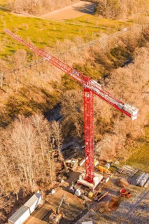 Red crane on a construction site, surrounded by autumnal forests and seen from the air,