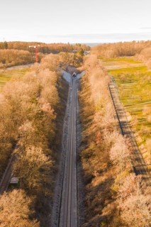 Aerial view of a train line through autumnal forests, parallel to a road, construction of the