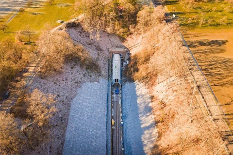Aerial view of a train line through an autumnal forest and open meadows, construction of the