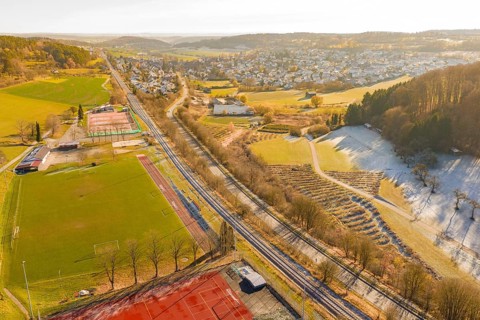 A railway traverses a scenic winter landscape with fields and a nearby village, construction of the