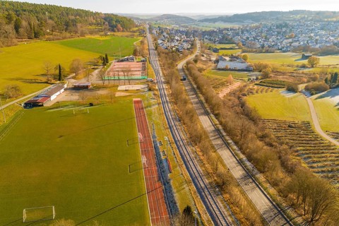 Aerial view of a railway bordering fields and a sports field in a rural area, construction of the