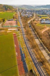 Railway line and road next to a sports field in a rural area, construction of the Hermann Hesse