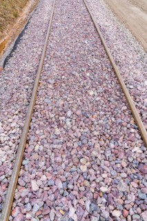 Detailed view of railroad tracks densely covered with grey and purple gravel, construction of the