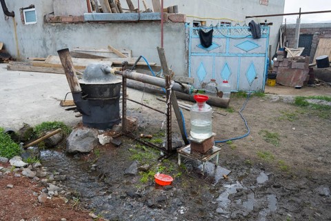 Self-built distillation plant in front of a rural farm with various materials, production of