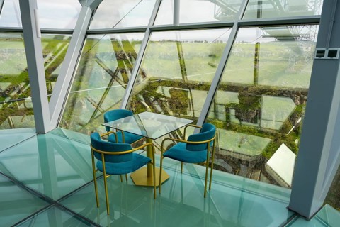 A stylish interior with glass floor and modern blue chairs offers an open view, Diamond Bridge,