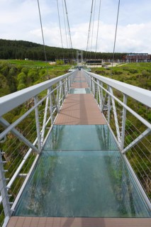 A modern suspension bridge with glass floor stretches across a green gorge, Diamond Bridge, Diamond