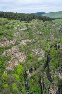 A green gorge with rocks and trees crossed by a small river under a cloudy sky, man riding a