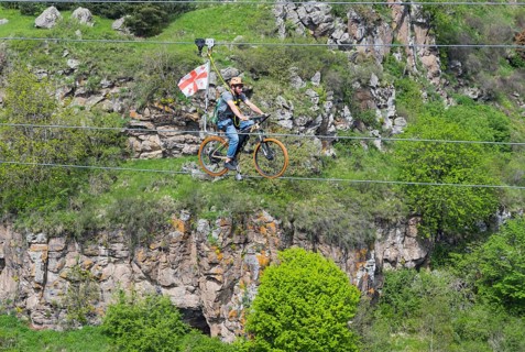 A person balances with a bicycle on a rope against a rocky backdrop, Dashbashi Gorge, Khrami River,