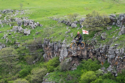 Person riding a bicycle on a stretched rope across a gorge in green countryside, Dashbashi Gorge,