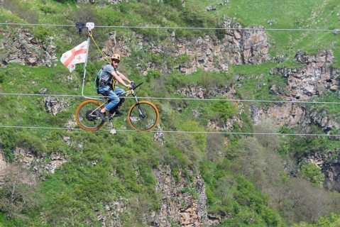 Man on a bicycle balancing at lofty heights above a green valley, Dashbashi Gorge, Khrami River,