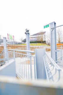 Entrance area with modern steel structure and flags, buildings in the distance, parking garage