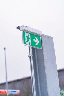 Green emergency exit sign with directional arrow on a metal post, parking garage construction with