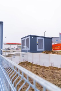 Shed on a fenced area with earthworks in the foreground, parking garage construction with charging