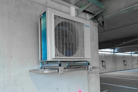 Air conditioner installed on an industrial bracket on a concrete wall indoors, parking garage
