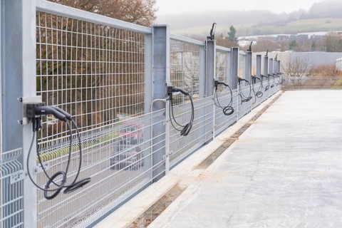 Cables run over a long fence on a concrete surface, with landscape in the background, parking