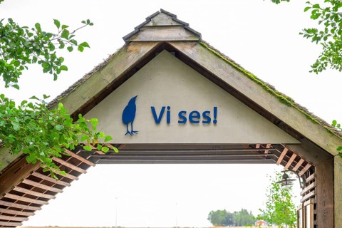 Welcome sign under a rustic wooden roof with green leaves, Vogelsee Tåkern, Vadstena,