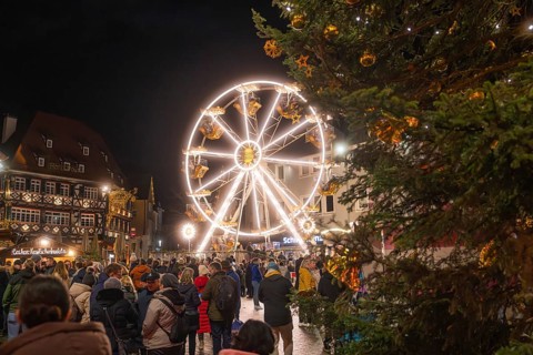 Illuminated Ferris wheel and half-timbered houses at night on a busy Christmas market,