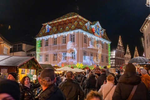 Lively scene at a market with light projection onto a building and people celebrating,