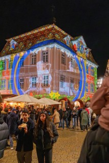 Artistic light projection onto a building at night, surrounded by people and a festive atmosphere,
