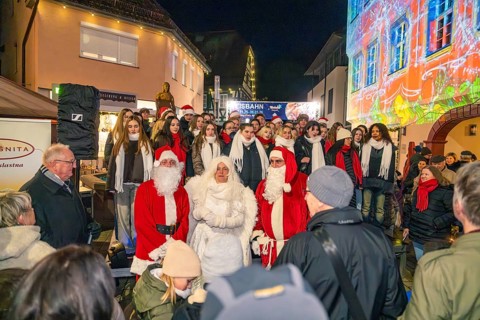 People wearing Christmas costumes at a night outdoor party surrounded by colorful lights,