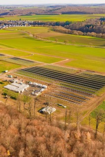 Large solar system next to buildings, surrounded by fields and forests, energy revolution,