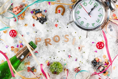 Letters cheers in the snow surrounded by lucky charms, watch and champagne bottle, New Year's Eve
