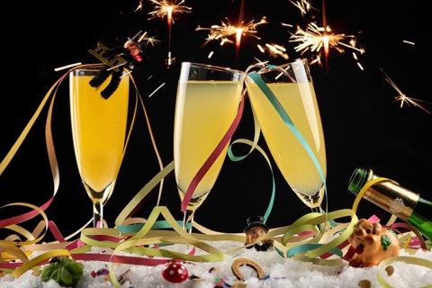 Sparks fly over three champagne glasses with lucky New Year's charms and streamers in the snow