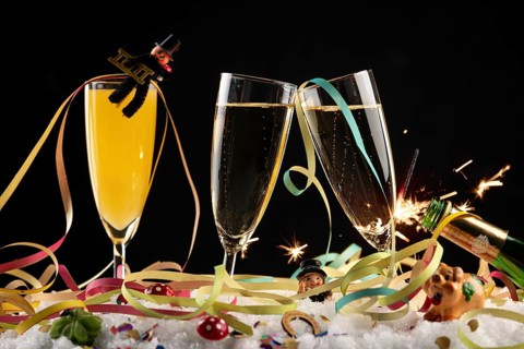 Three champagne glasses with lucky charms for New Year, streamers and sparkler in the snow