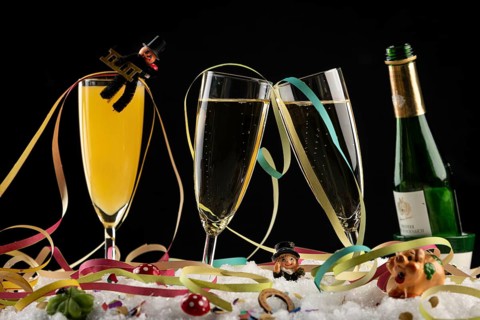 Champagne bottle, glasses with sparkling wine, streamers and lucky charms in the snow