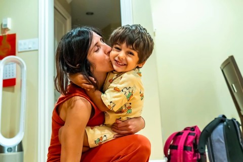 Happy mother kissing her cheerful son on the cheek while holding him in her arms, enjoying a warm
