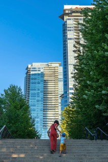 Mother and son climbing stairs together, surrounded by towering skyscrapers and lush trees in
