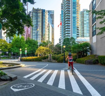 Canadian flag waving between modern buildings while a woman with backpack and helmet rides her