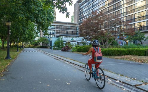 Woman with backpack and helmet is riding a bicycle on a dedicated bike lane next to a park,