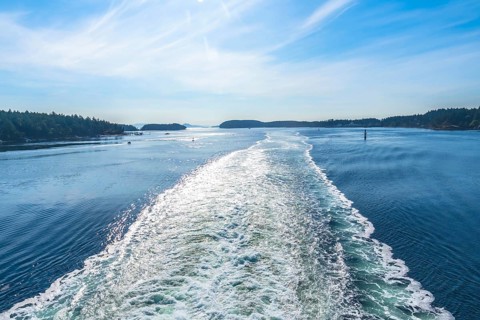 Sparkling ocean water reflects sunlight in the wake of a ferry traveling between islands near