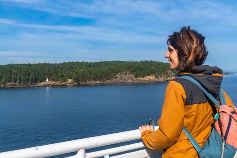 Tourist leaning on the ferry railing, enjoying breathtaking ocean views and a small island with a